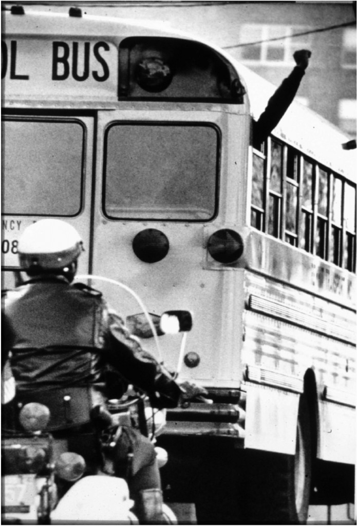 A black student raises a fist while Police  protect school buses in Boston, MA, in 1974 during forced busing to racially integrate schools. Peter Bregg/AP